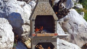A stone-built outdoor fireplace with a fire burning inside, surrounded by large rocks and a stone-paved area. - Fantastisches Haus nur 700m vom Strand entfernt by Interhome (Rab/Kampor)