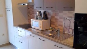 A modern kitchen with white cabinets, a microwave, a kettle, and a black oven. - in Kampor mit Privatparkplatz by Interhome (Rab/Kampor)