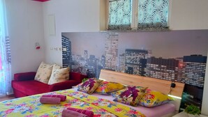 Ein Schlafzimmer mit Stadtbild-Wandgemälde, einem roten Sofa, einem Bett mit floralem Bettzeug und einem Nachttisch mit Pflanze.