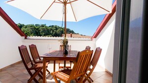 Um pátio com mesa e cadeiras, um guarda-sol grande e vista para uma paisagem verde.
