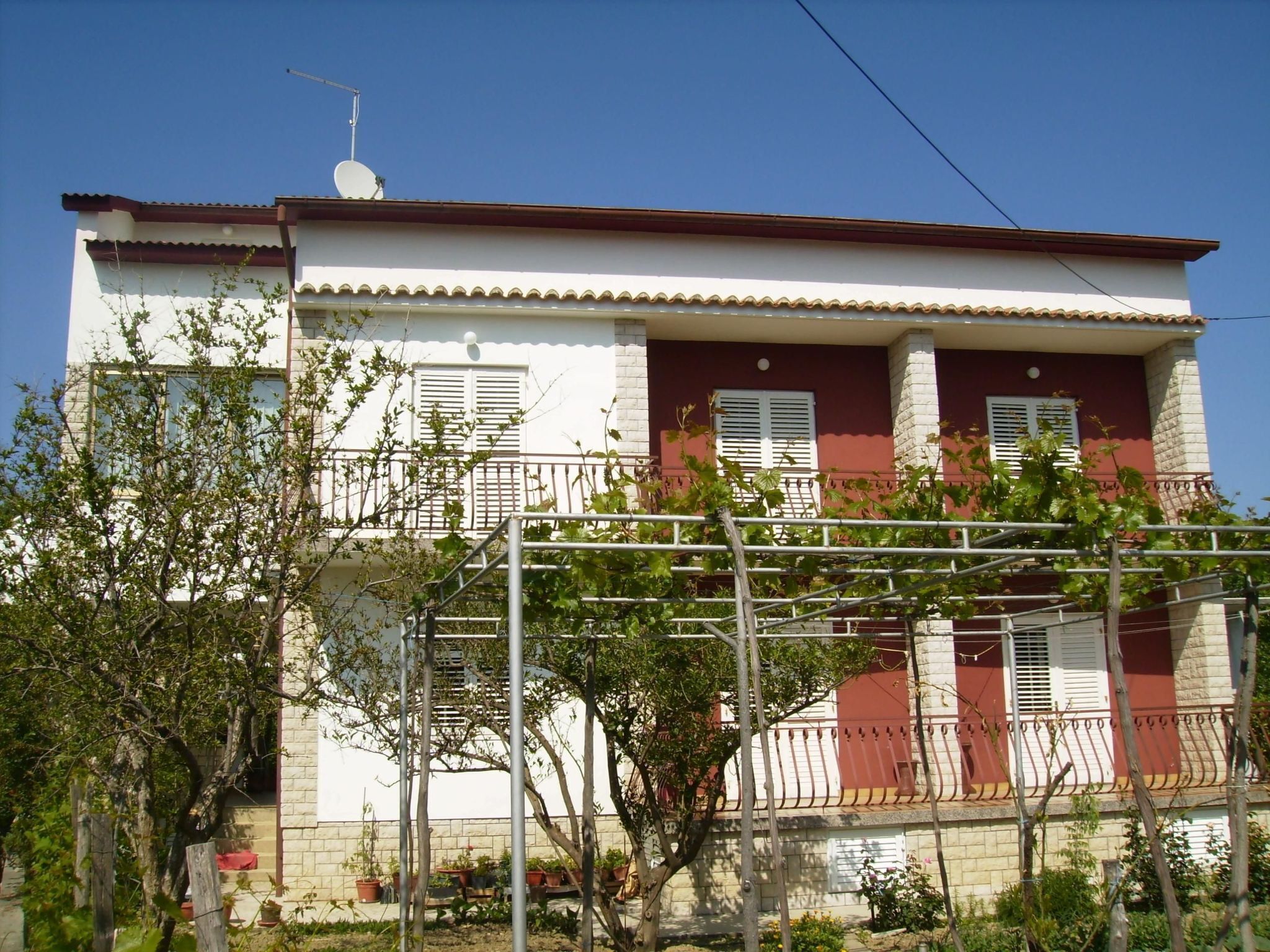 A two-story building with a balcony, a satellite dish, and a garden area with potted plants.
