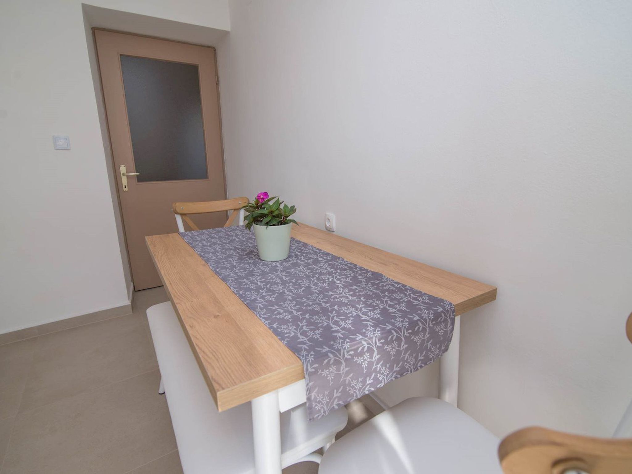 A small dining table with a floral tablecloth, a potted plant, and a wooden chair.
