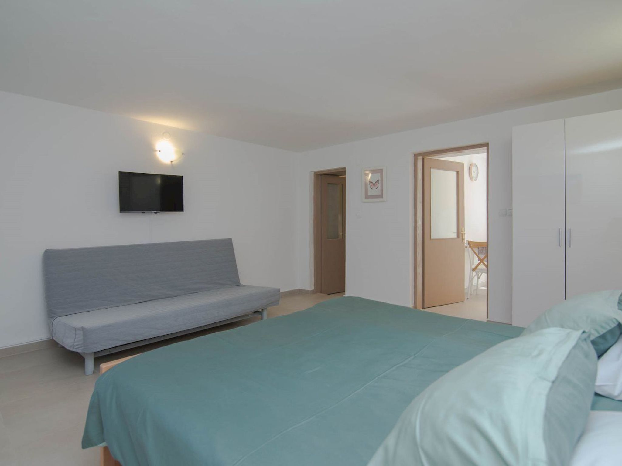Een slaapkamer met een bed, een bank, een televisie en een kledingkast.