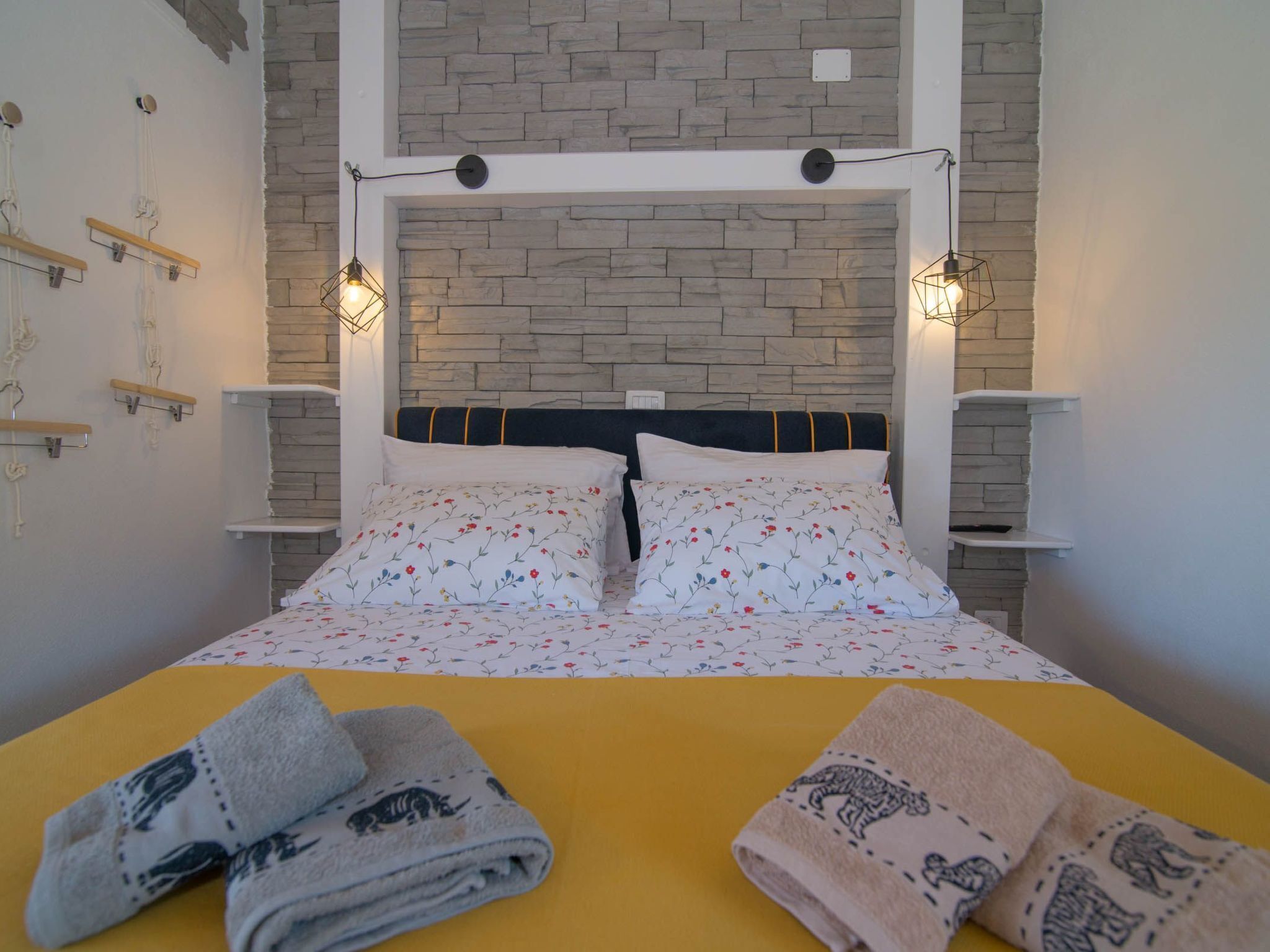 Ein Bett mit floraler Bettwäsche, ein Kopfteil vor einer Wand aus Stein, und zwei Nachttischlampen.