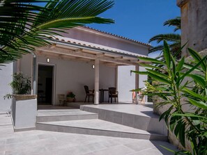 Un patio techado al aire libre con suelo de piedra, una pérgola y una zona de estar con sillas.