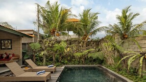 Un área de piscina con sillas de descanso, un muro de piedra y plantas tropicales.