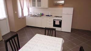 Eine kleine Küche mit weißen Schränken, einem Gasherd, einem Backofen und einem Fenster mit Vorhängen.