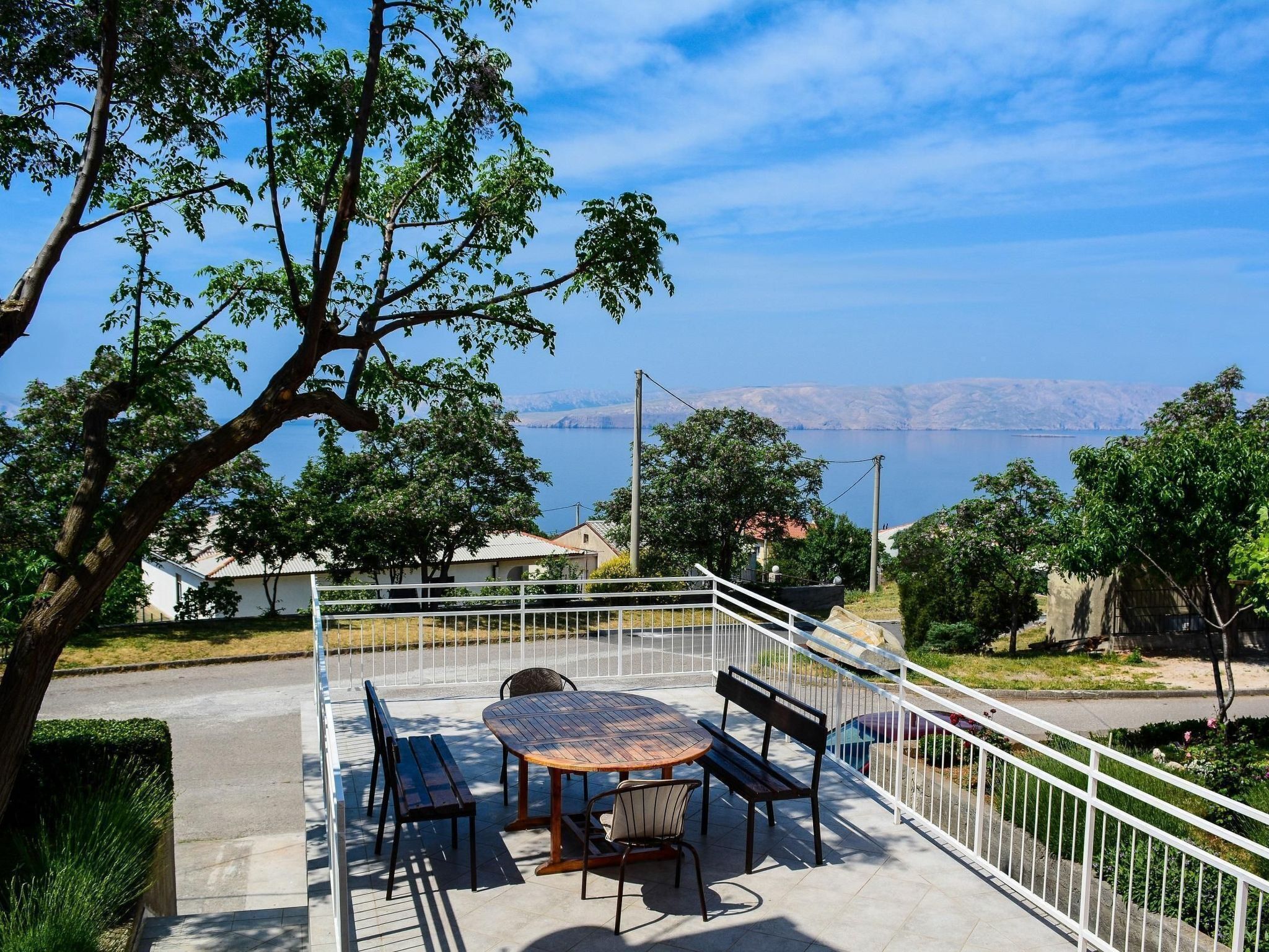 A terrace with a table and benches overlooking a scenic view of a lake and distant mountains.