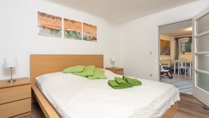 Un letto rifatto con cuscini verdi e una coperta bianca in una stanza con pavimento in legno e pareti bianche.