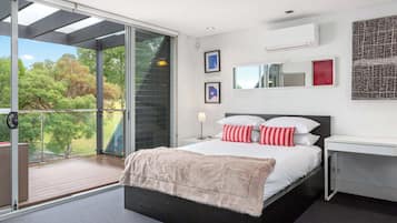 Un dormitorio moderno con una cama grande, un escritorio y un balcón con vistas a árboles.
