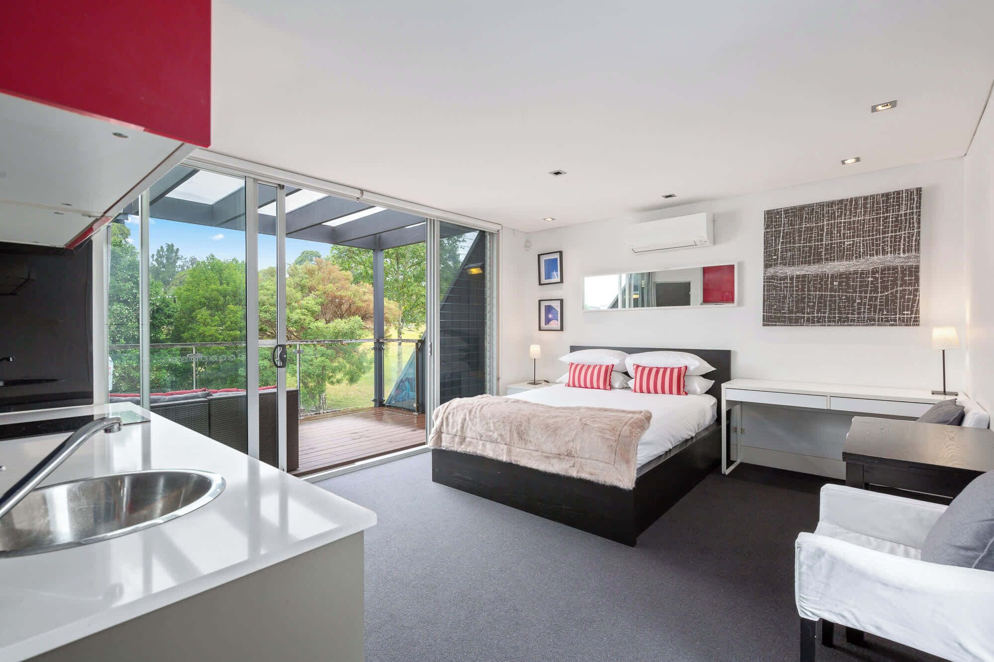 Un dormitorio moderno con una cama grande, un escritorio y un balcón con puertas de cristal.