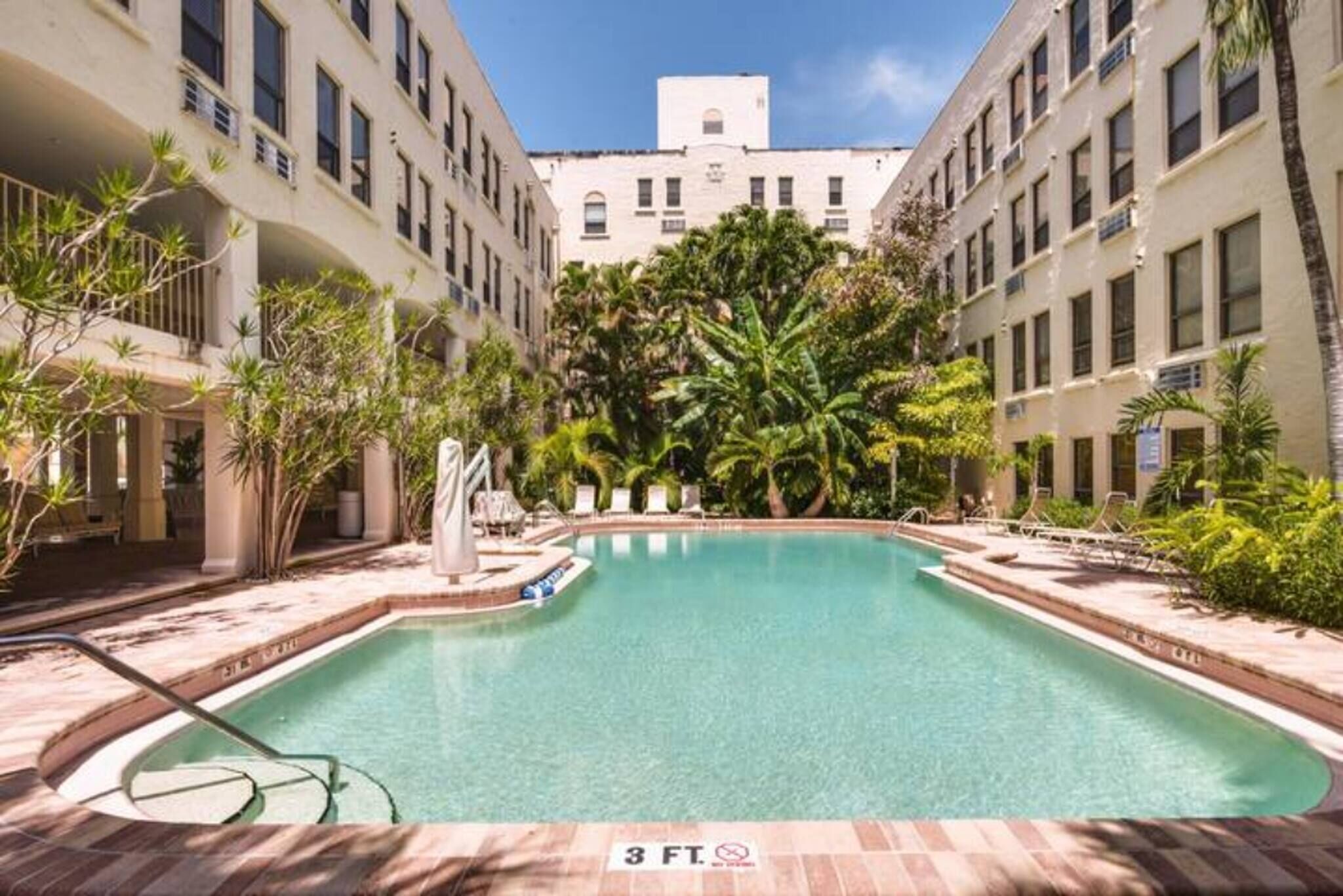Una piscina rodeada de edificios, palmeras y sillas de descanso.