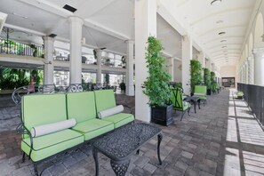 A covered outdoor seating area with a green sofa, a table, and potted plants. - Special/Pool/StepsToBeach/Terrace Studio (Palm Beach)
