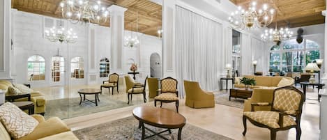 A spacious lobby with high ceilings, chandeliers, and a mix of seating arrangements including sofas and armchairs.