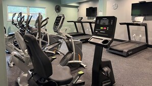 A gym with multiple exercise machines, a TV, and a window with a view of trees. -  Spacious 3-bed, 2-bath condo with large all-season patio & optional Boat Slip. (Lake Ozark)
