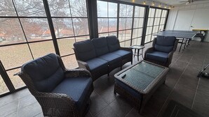 A spacious room with large windows, wicker furniture, and a ping pong table. -  Spacious 3-bed, 2-bath condo with large all-season patio & optional Boat Slip. (Lake Ozark)