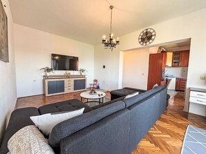 A modern living room with a sofa, TV, chandelier, and a kitchen in the background. - Schöne Wohnung in Dramalj by Interhome (Crikvenica/Dramalj)