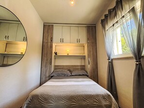 A bedroom with a bed, a mirror, a wardrobe, a shelf with a lamp, and a window with curtains. - Schöne Wohnung in Dramalj by Interhome (Crikvenica/Dramalj)