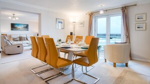 Un moderno comedor con vista al mar, con una mesa blanca adornada con sillas anaranjadas, un sofá blanco y un sillón blanco.