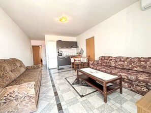A living room with a sofa, a coffee table, and a kitchen in the background. - Appartement in Dramalj mit Möbliertem Balkon by Interhome (Crikvenica/Dramalj)