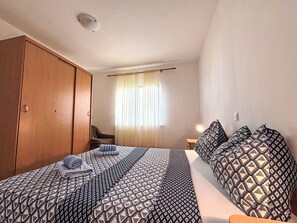 A bedroom with a bed, a wardrobe, a chair, and a window with curtains. - Appartement in Dramalj mit Möbliertem Balkon by Interhome (Crikvenica/Dramalj)