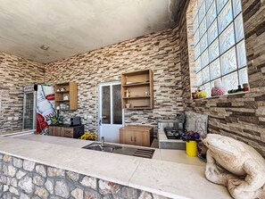 A kitchen with a stone wall, a sink, wooden cabinets, a stove, and a decorative frog statue. - Wohnung in Dramalj mit Möbliertem Balkon by Interhome (Crikvenica/Dramalj)