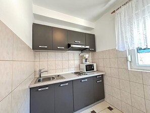 A compact kitchen with dark cabinets, a microwave, a coffee maker, and a window with curtains. - Wohnung in Dramalj mit Möbliertem Balkon by Interhome (Crikvenica/Dramalj)
