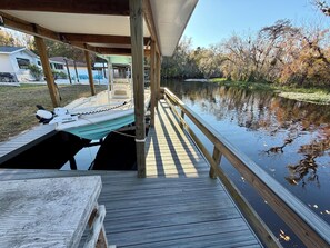 A wooden dock extending over a calm body of water, with a boat docked on the left and a covered area on the right. - On scenic blue creek, newly renovated close to springs and forest (Astor)