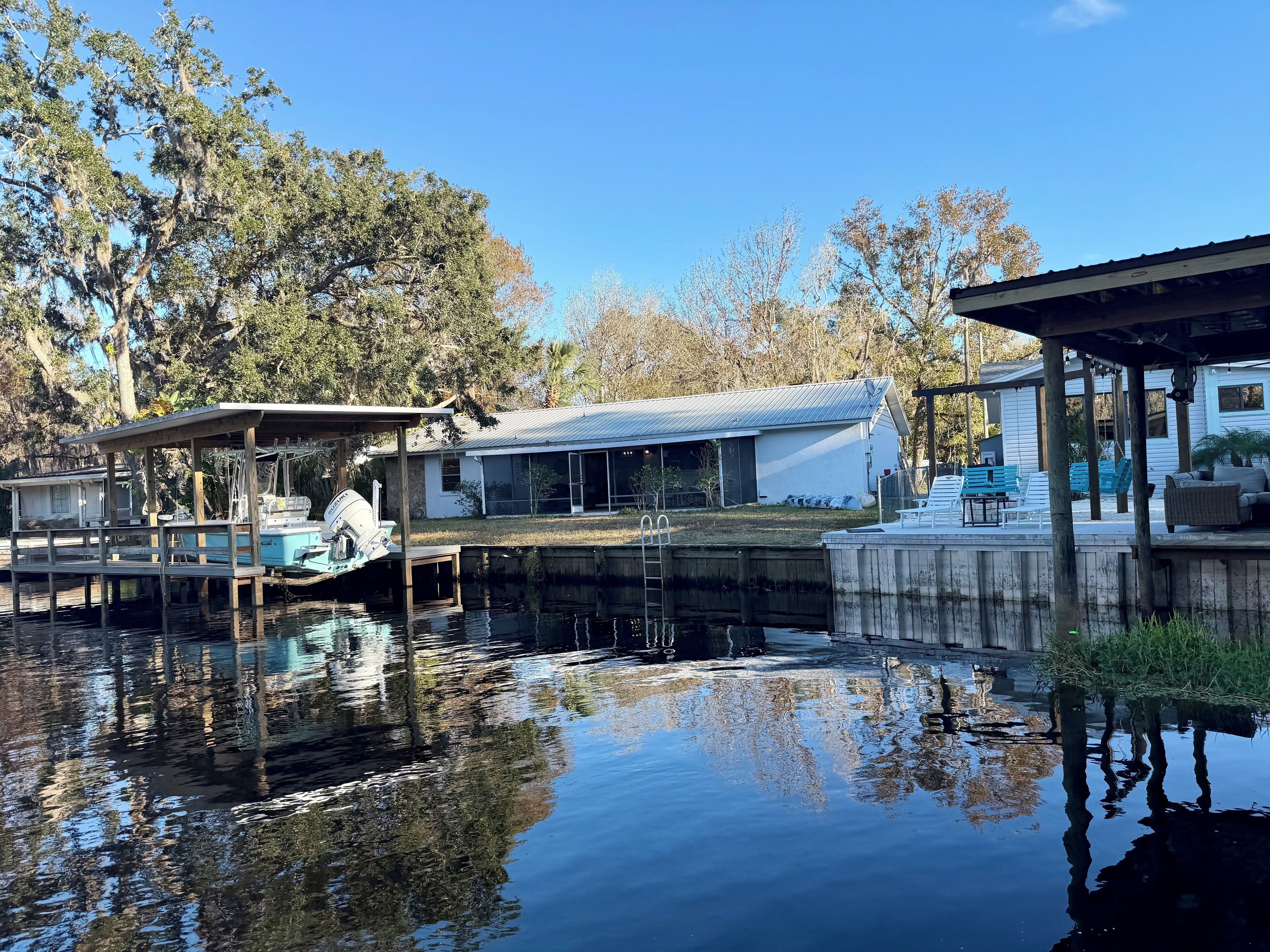 A waterfront property with a dock, a covered boat house, and a house with a large window overlooking the water.