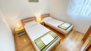 A twin room with two single beds, wooden headboards, bedside tables with lamps, and a window with sheer curtains. - Appartement in Jadranovo mit Terrasse by Interhome (Crikvenica/Jadranovo)