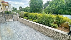 A rooftop terrace with a gravel surface, a brick retaining wall, and a variety of green shrubs and trees in the background. - Appartement in Jadranovo mit Terrasse by Interhome (Crikvenica/Jadranovo)