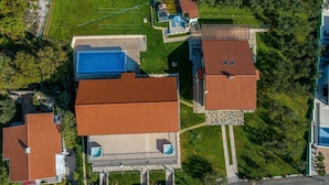 Vista aerea di una zona residenziale con diverse case, ognuna con un tetto in tegole rosse e una piscina.
