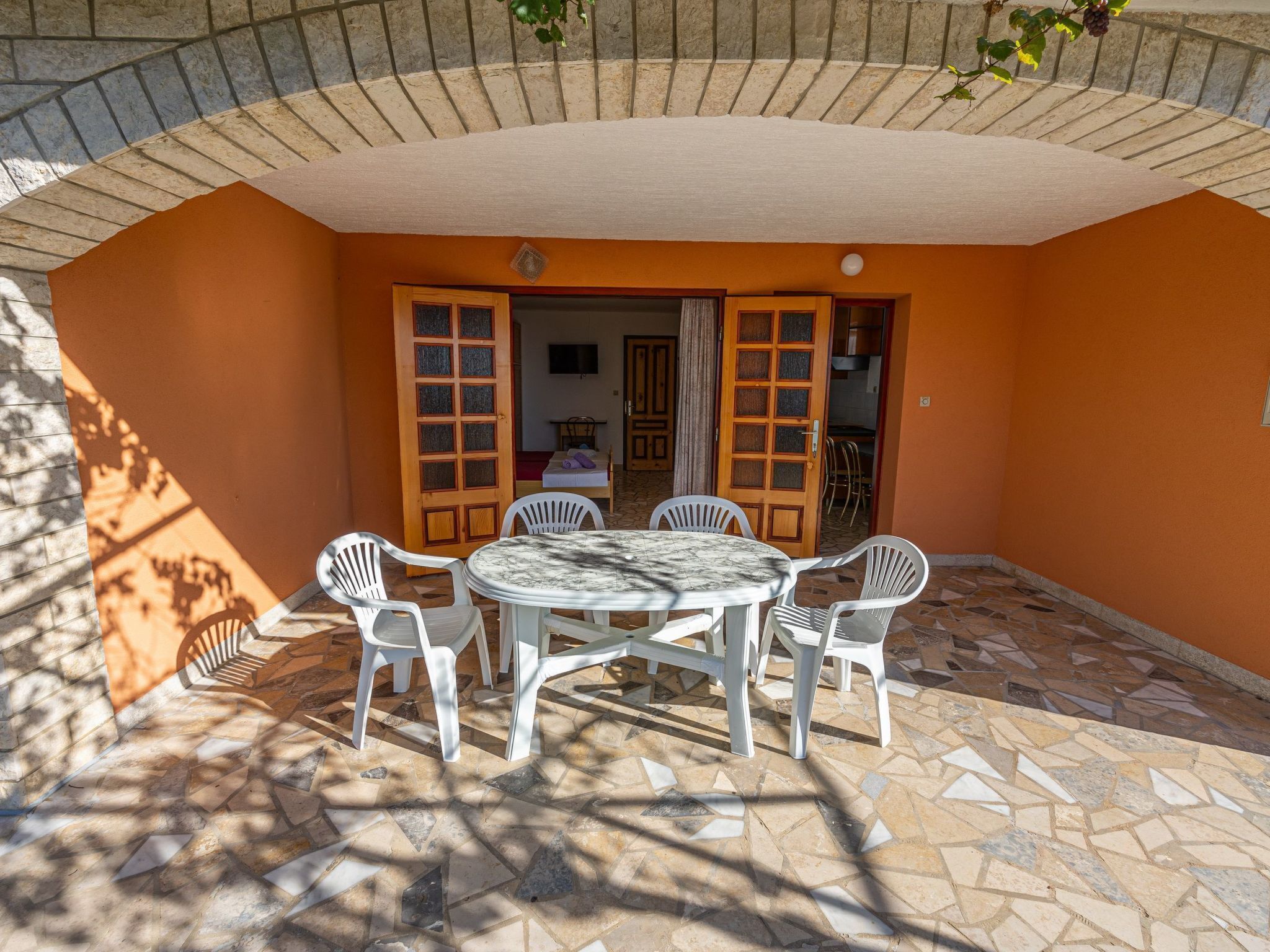 An outdoor patio with a round table and white plastic chairs, surrounded by orange walls and a tiled floor.