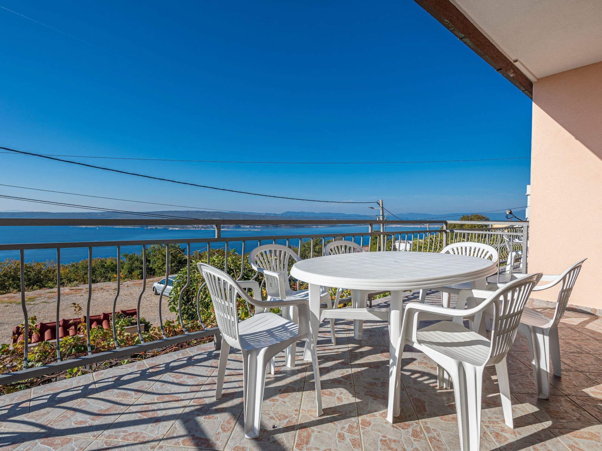 A terrace with a round table and chairs, overlooking a coastal view.