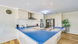 A modern kitchen with white cabinets, a blue countertop, a gas stove, a sink, and a stainless steel refrigerator. - StayAU Comfortable House w/Pool Table & Backyard (Corio)