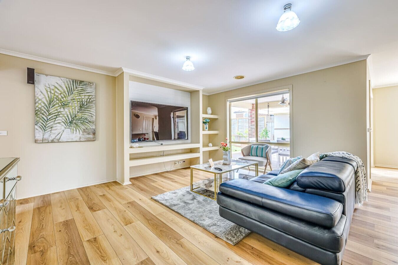 A spacious living room with a black leather sofa, a coffee table, and a large window providing natural light.