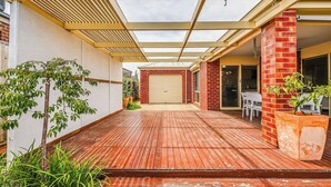 A covered patio area with a wooden deck, a brick wall, and a garage door. - StayAU Comfortable House w/Pool Table & Backyard (Corio)
