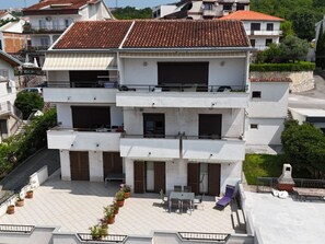 Un immeuble à plusieurs étages, doté d’un toit recouvert de tuiles, de balcons et d’une terrasse aménagée avec du mobilier d’extérieur.