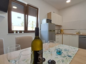 A modern kitchen with a dining table set for two, a bottle of wine, and a glass of water. - in Crikvenica mit Meerblick by Interhome (Crikvenica)