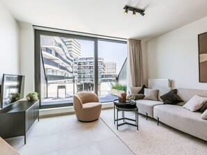 A modern living room with a large window, a sofa, a chair, and a small table. - Bel Air with parking and balcony by Interhome (Oostende)
