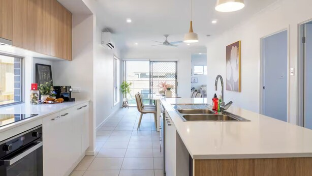 Une cuisine moderne avec des meubles blancs, un grand îlot central doté d’un évier et un ventilateur de plafond.