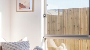 Une chambre moderne avec une grande fenêtre, un canapé gris et deux œuvres d’art encadrées accrochées au mur.
