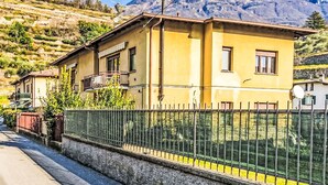 Ein gelbes Gebäude mit Balkon, Zaun und Bergen im Hintergrund.