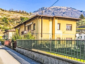 Ein gelbes Gebäude mit Balkon, Zaun und Bergen im Hintergrund.