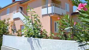 Un edificio a due piani con balconi, un recinto bianco e vegetazione.