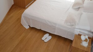 Un letto rifatto con una coperta bianca, un armadio in legno e un comodino con una lampada.