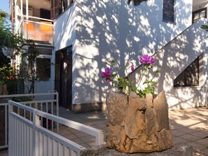 A stone planter with flowers in front of a building with a white facade and a balcony. - Wohnung "Petar 2" direkt am Strand by Interhome (Krk/Milohnići)