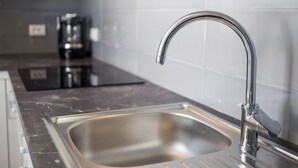 Una cocina moderna con un lavamanos de acero inoxidable, una placa de cocción por inducción negra y paredes con azulejos blancos.