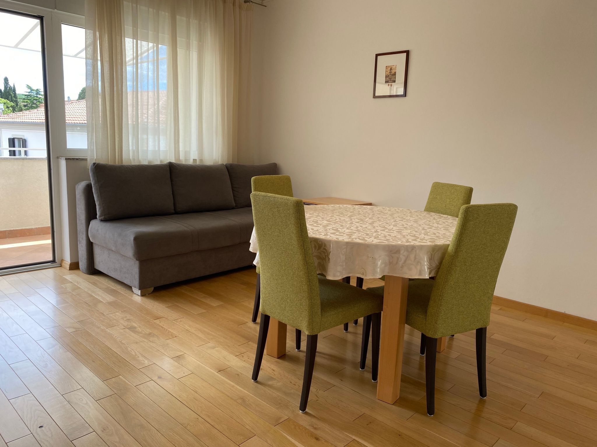 A dining area with a table and four chairs, a sofa, and a window with curtains.