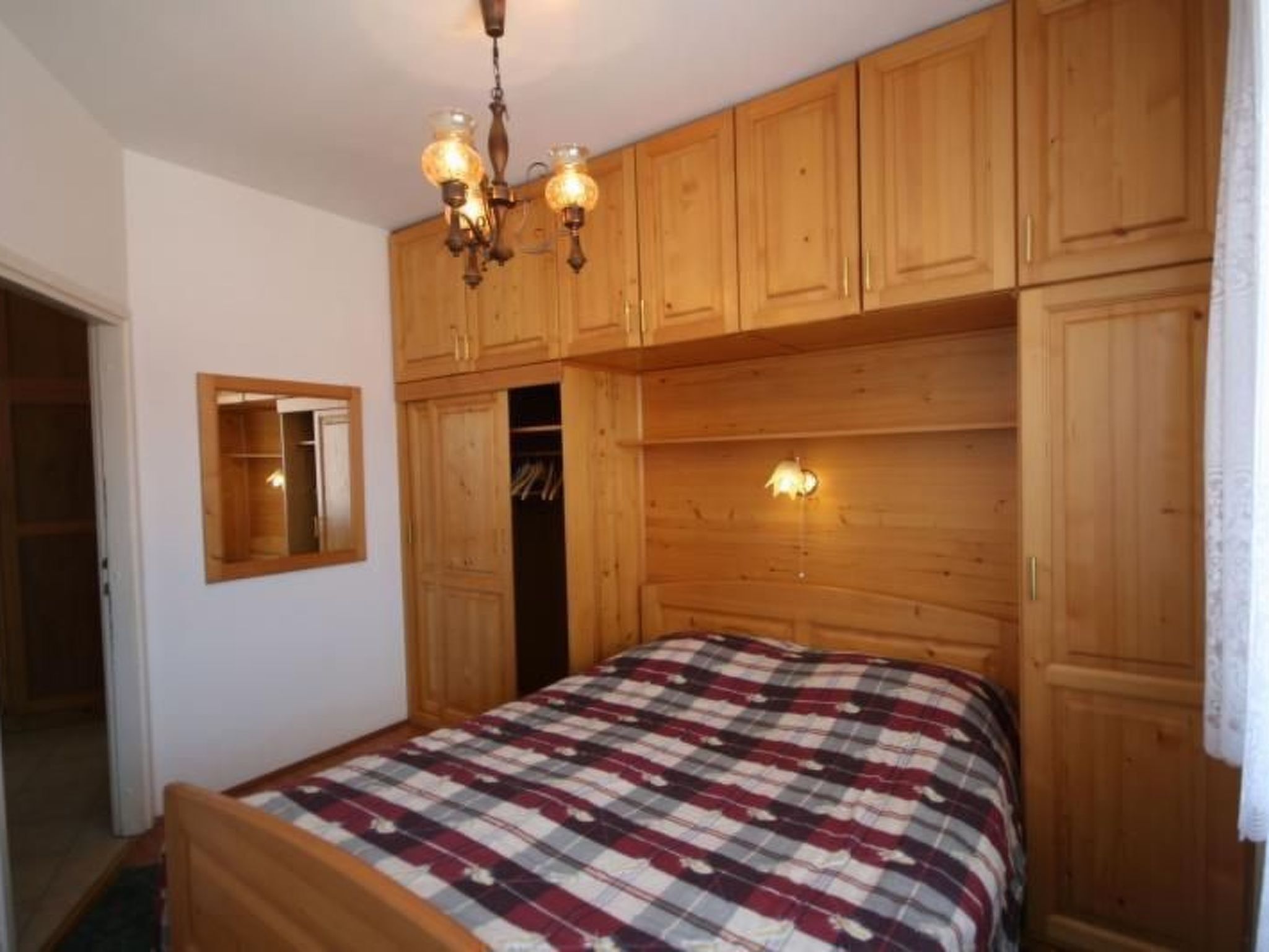 Un dormitorio con armarios de madera, una cama con colcha escocesa, una araña y un espejo en la pared.